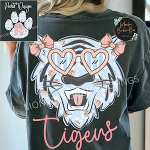 May include: Dark gray t-shirt featuring a tiger design with heart-shaped sunglasses and pink bows. The tiger has a floral pattern and the word "Tigers" in pink script. A paw print design is on the upper left.