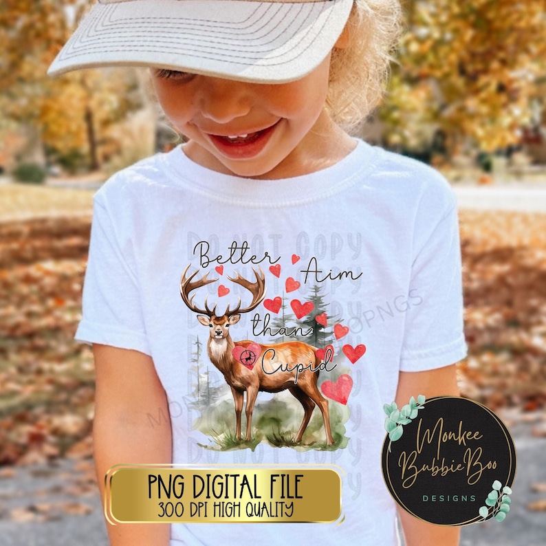May include: A white t-shirt with a watercolor illustration of a deer with a target on its back. The text "Better Aim than Cupid" is written above the deer. The image is surrounded by red hearts.