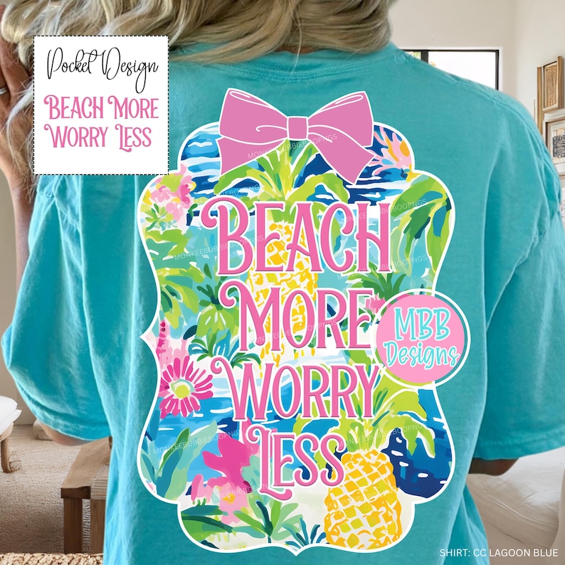 May include: A turquoise t-shirt featuring the text "Beach More Worry Less" in a colourful design with pineapples and tropical elements. The shirt has a relaxed fit and a pink bow at the top of the design.