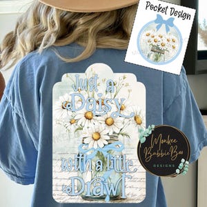May include: A blue t-shirt with a white and blue design featuring a mason jar filled with daisies and the text "Just a Daisy with a little Drawl".