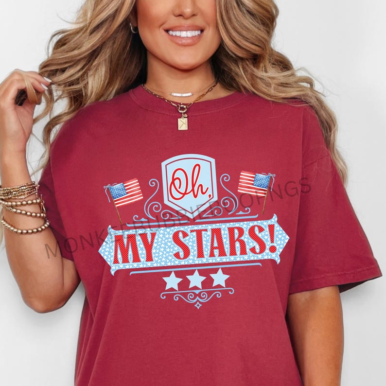 May include: Red t-shirt with a graphic design featuring a blue and white shield with the text "Oh, My Stars!" and two American flags. The shield is decorated with a blue and white star pattern.