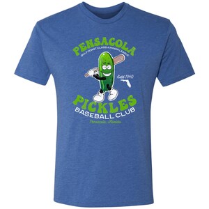 May include: A blue t-shirt featuring a cartoon pickle holding a baseball bat. The text on the shirt reads "Pensacola Gulf Coast Class-A Minor League Estd 1940 Pickles Baseball Club Pensacola, Florida."