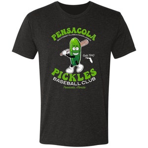 May include: A dark heather grey t-shirt featuring a cartoon pickle holding a baseball bat. The text "Pensacola Gulf Coast Class A Minor League Estd 1940 Pickles Baseball Club Pensacola, Florida" is printed on the shirt.