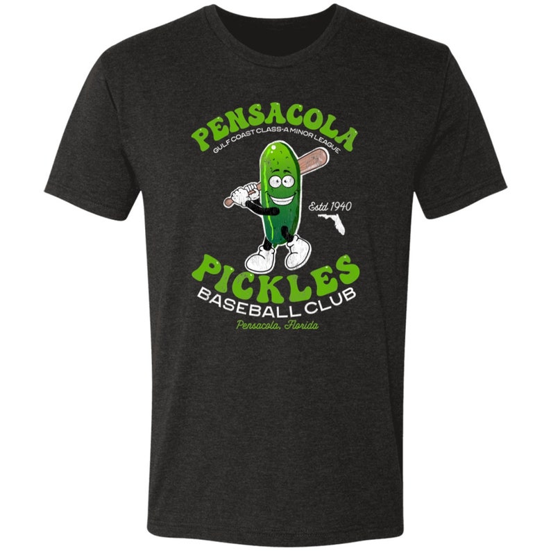 May include: A dark heather grey t-shirt featuring a cartoon pickle holding a baseball bat. The text "Pensacola Gulf Coast Class A Minor League Estd 1940 Pickles Baseball Club Pensacola, Florida" is printed on the shirt.