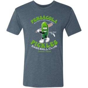 May include: A blue t-shirt featuring a vintage-style graphic of a cartoon pickle holding a baseball bat. The graphic reads "Pensacola Gulf Coast Class-A Minor League Pickles Baseball Club Pensacola, Florida Est. 1940".