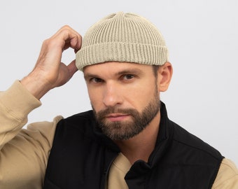 May include: A beige knitted beanie with a folded brim. The beanie is made of a soft, comfortable material and has a relaxed fit.