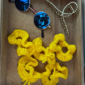 May include: A wooden box with a pair of blue round sunglasses and yellow crocheted hair scrunchies.