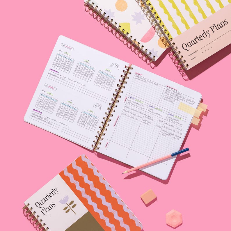 Quarterly Plans 90-Day Planner shown open to quarterly overview pages with the Tulip Wave cover design and planning accessories on a pink background.