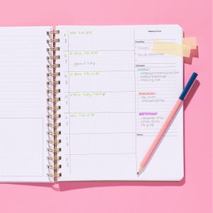 Quarterly Plans weekly page spread with space for weekly focus, priorities, checklist, and notes, shown open on a pink background with a pencil.