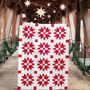 May include: A red and white quilt with a snowflake pattern. The quilt is hanging on a wooden structure with a railing.