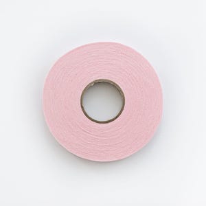 May include: A roll of pink fabric tape, viewed from above, against a white background. The tape is tightly wound, revealing a central cardboard core. The pink color is soft and consistent throughout the roll.