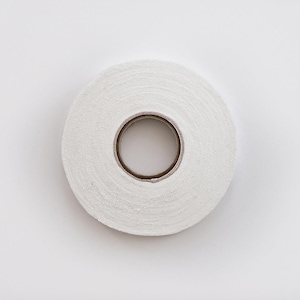 May include: A roll of white athletic tape, seen from above, against a white backdrop. The tape is tightly wound, with a brown cardboard core visible. The tape's texture appears slightly rough.