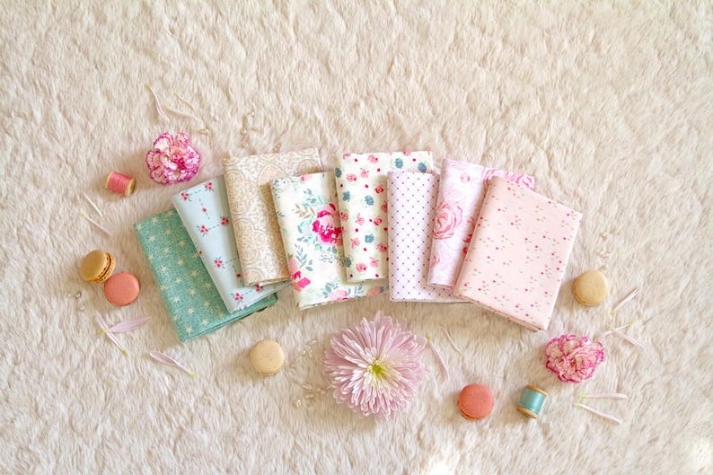 Puede incluir: Vista a&eacute;rea de varias telas con estampados florales y de lunares en colores pastel. Las telas est&aacute;n dispuestas con macarons, flores y carretes de hilo sobre una superficie blanca texturizada. Una colecci&oacute;n de suministros de artesan&iacute;a.