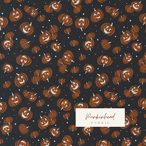 May include: A black fabric with a repeating pattern of orange jack-o'-lantern faces. The fabric has a white label with the text "Pumpkinhead Fabric".