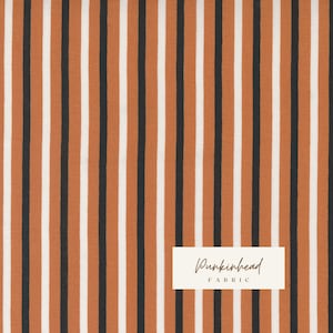 May include: A fabric with alternating stripes of black, white, and orange. The fabric is labelled "Pumpkinhead Fabric".