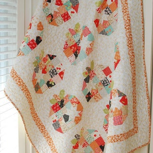 May include: A white quilt with a patchwork design featuring multiple colorful pumpkins. The quilt has a white background with orange and white borders.