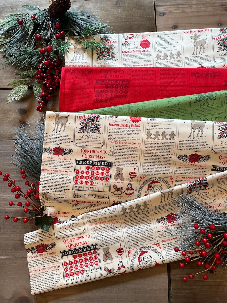 May include: A cream-colored fabric featuring a repeating Christmas-themed newspaper print with red and black text, illustrations of Santa, reindeer, gingerbread men, and a December calendar. The design includes sections titled Deck the Halls.