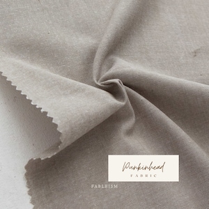 May include: Close-up of a beige fabric with a slightly textured surface. The fabric is folded and draped, showcasing its soft and drapey quality. The text "Pumpkinhead Fabric" is visible in the lower right corner.