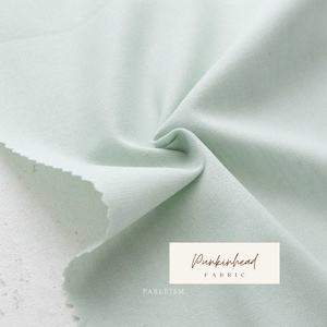 May include: A close-up of a light green fabric with a textured surface. The fabric is folded and draped, showing its soft and drapey texture. The text "Pumpkinhead Fabric" is visible in the lower right corner of the image.