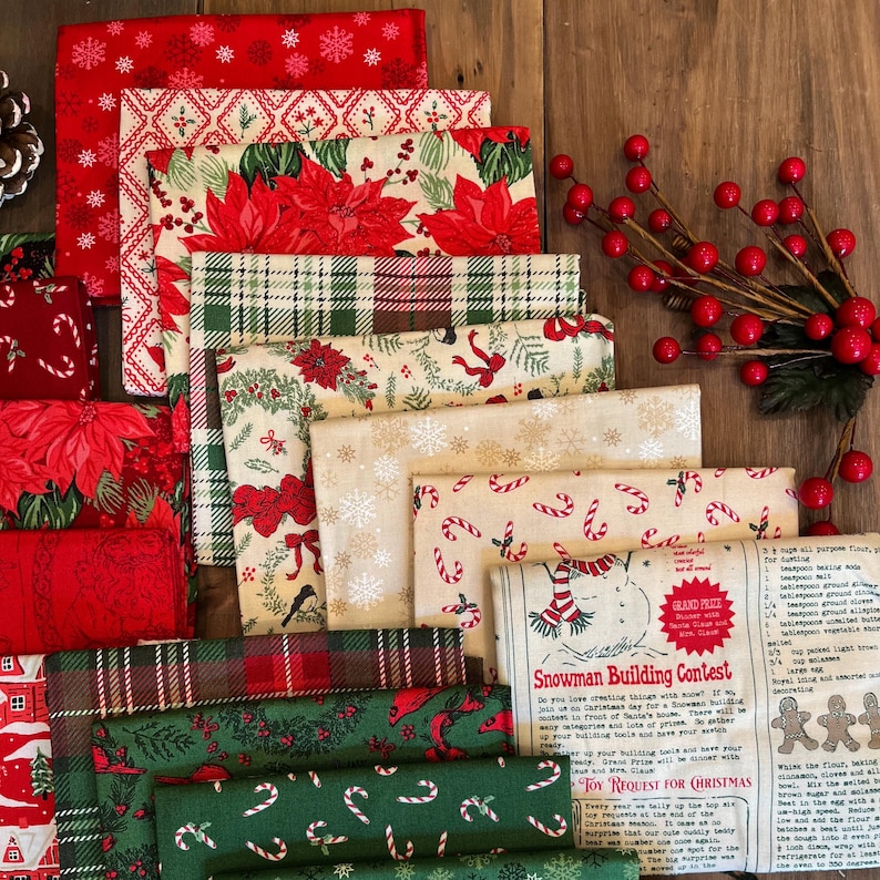 May include: A collection of folded fabric squares featuring Christmas patterns including red poinsettias, green plaid, candy canes, snowflakes, and a cream-colored panel with text titled Snowman Building Contest and a recipe for gingerbread.