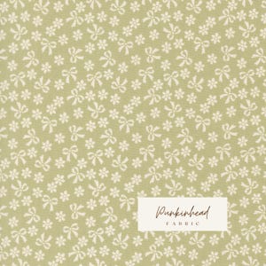 May include: A sage green fabric featuring a repeating pattern of small white flowers and bows. A white rectangular label is overlaid on the bottom right corner, displaying the text Punkinhead FABRIC in a dark brown script and sans-serif font.
