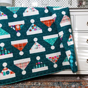 May include: A teal blue quilt with a white and red Christmas hat pattern. The quilt has a white border and the words "Merry Merry Merry" are printed on the quilt.