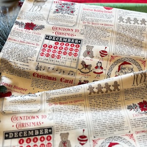 May include: A cream-colored fabric featuring a repeating Christmas-themed newspaper print in red and black ink. The design includes a December calendar, gingerbread men, a Santa Claus illustration, and various holiday-themed text sections.