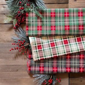 May include: Three folded pieces of fabric featuring distinct plaid patterns in red, green, and white. The top fabric is green with red and white lines, the middle is white with red and green lines, and the bottom is dark gray with red lines.