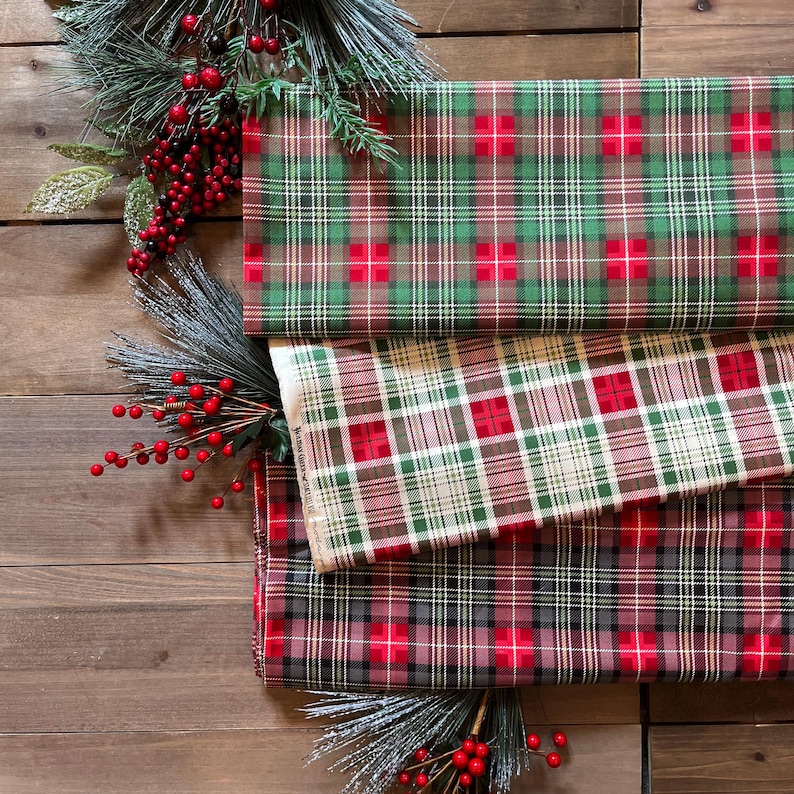 May include: Three folded pieces of fabric featuring distinct plaid patterns in red, green, and white. The top fabric is green with red and white lines, the middle is white with red and green lines, and the bottom is dark gray with red lines.