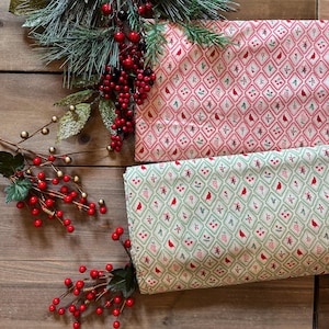 May include: Two folded pieces of fabric featuring a diamond grid pattern. One piece has a red background with white and green accents, while the other has a light green background with red and white accents. Both fabrics display small red birds.