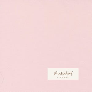 May include: A pale pink fabric with a textured surface. The fabric has a uniform colour and a slight sheen. The words "Punkinhead FABRIC" are printed on a rectangular label in the lower right corner.