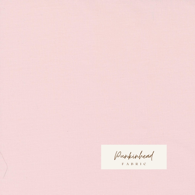 May include: A solid light pink fabric with a subtle textured appearance. The fabric has a soft, even color and a slight sheen. The words "Punkinhead FABRIC" are printed on a rectangular label in the lower right corner.