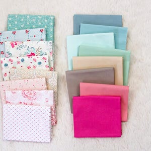 Puede incluir: Montones de cuadrados de tela en varios colores y patrones. La pila izquierda presenta dise&ntilde;os florales y de lunares en rosa, blanco y azul claro. La pila derecha incluye telas lisas en tonos de azul, rosa y beige.