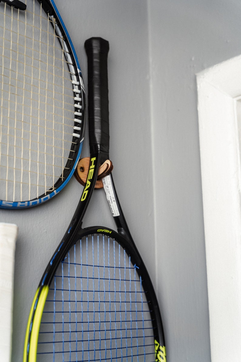 May include: Two tennis rackets hanging on a wall. The racket on the left is blue and white. The racket on the right is black with yellow accents and the word "HEAD" printed on it.
