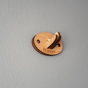 May include: A wooden wall hook with the word "Winner" engraved on it. The hook is oval shaped and has a light brown color.