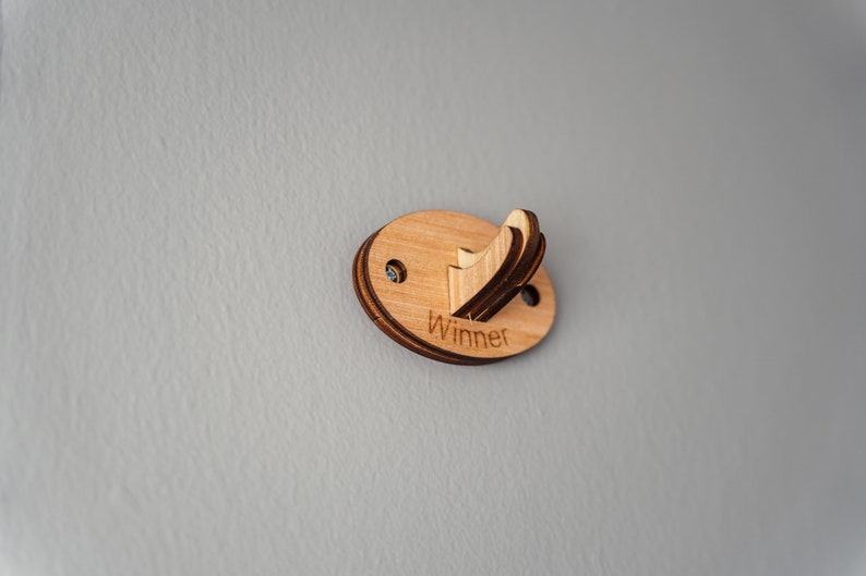 May include: A wooden wall hook with the word "Winner" engraved on it. The hook is oval shaped and has a light brown color.