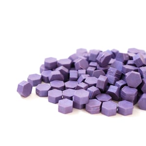 May include: A pile of purple wax seals, shaped like hexagons, are scattered on a white surface.