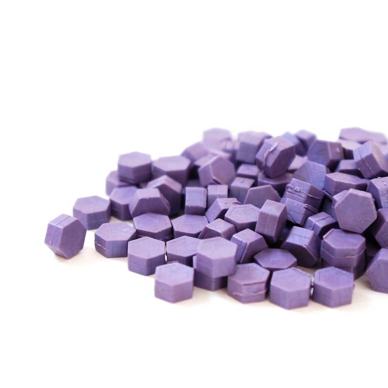 May include: A pile of purple wax seals, shaped like hexagons, are scattered on a white surface.
