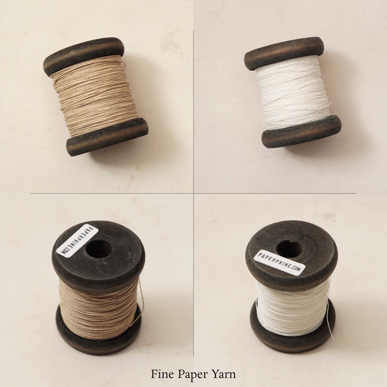 Puede incluir: Dos carretes de hilo de papel fino, uno blanco y otro beige natural, sobre un fondo blanco. Los carretes son de madera y tienen etiquetas con el texto "PAPERPHINE.COM" y "MADE IN THE USA".