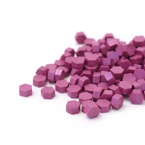 May include: A pile of purple wax seals, hexagonal in shape, scattered on a white surface.