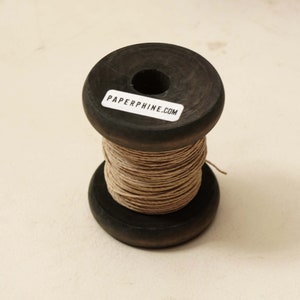 Puede incluir: Una bobina de hilo marr&oacute;n natural enrollada alrededor de una bobina de madera. La bobina tiene una etiqueta que dice "PAPERPHINE.COM".