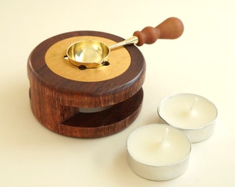 May include: A wooden wax seal stamp set with a brass spoon and two white tealight candles. The wooden base has a gold ring around the top.