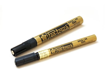 May include: Two gold paint markers with black caps. The larger marker is labeled "Pen-touch GOLD/OR ORO 2.0mm Medium Paint"
