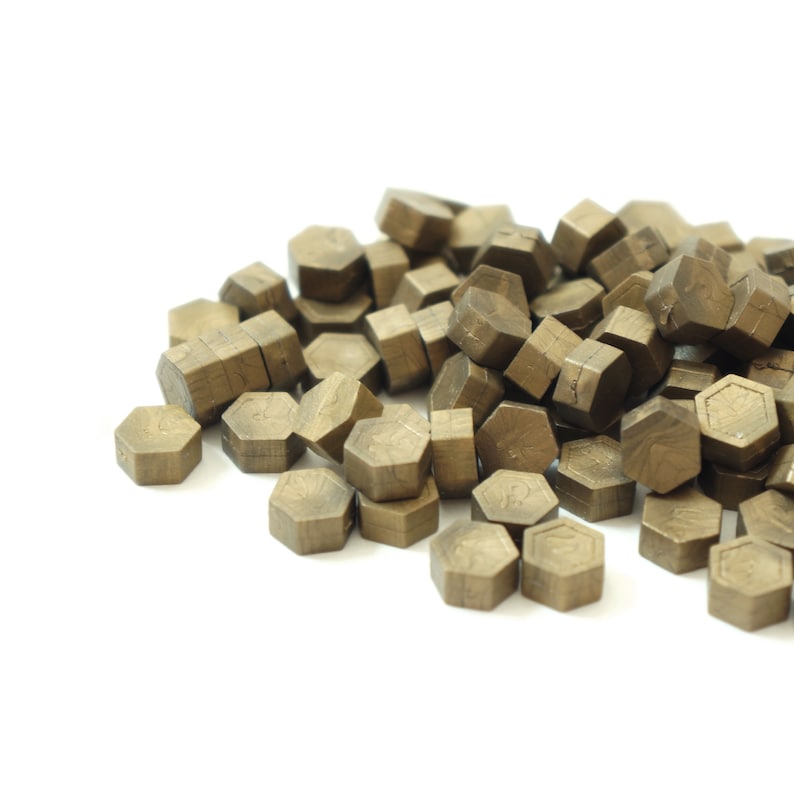 May include: A pile of hexagonal wax seals in a gold color. The seals are made of wax and are used to seal envelopes or other items.