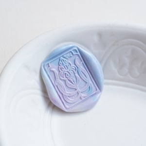 May include: A purple and blue wax seal with a floral design and the text "7016" in the center.