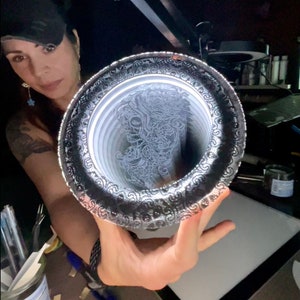 May include: A silver tray with a decorative border and a white, intricate design of a woman's face inside.