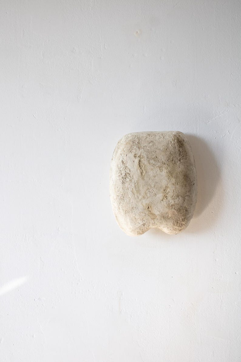 May include: A textured, off-white, rectangular sculpture with rounded edges and a slightly irregular surface. The sculpture has a rough, aged appearance, suggesting a natural or weathered material. The piece is set against a plain white background.