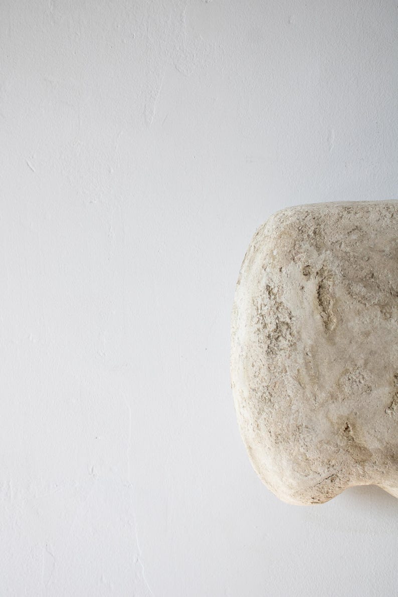 May include: A light beige, textured, rounded object against a white background. The object has a rough, uneven surface with a natural, organic appearance. The shape is smooth and curved.
