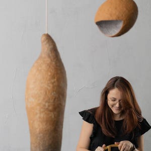 May include: Two hanging pendant lights with textured, organic shapes. One is elongated and teardrop-shaped, the other is a rounded oval with a gray interior. The lights are suspended from the ceiling by thin white cords. The overall theme is modern home decor.