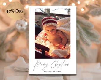 May include: A Christmas card featuring a baby wearing a red and white striped hat, sitting in a white blanket with Christmas lights. The card reads "Merry Christmas" with a handwritten font and "With Love, The Axtell's" below.